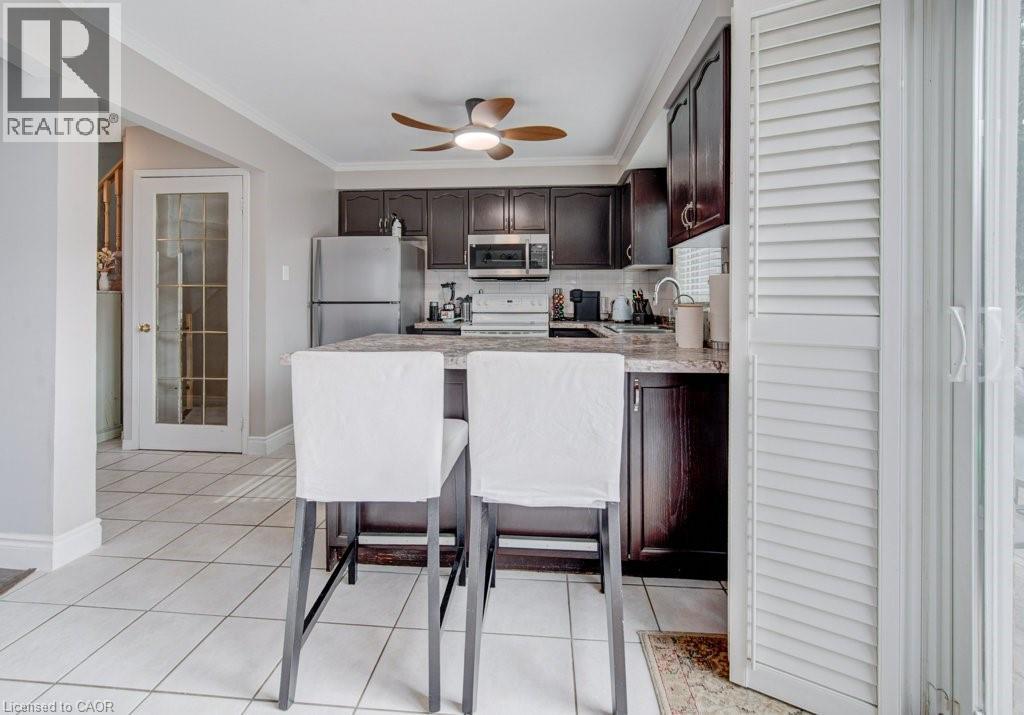 Kitchen featuring dark wood cabinetry, stainless steel appliances, a breakfast bar, and light-toned tile flooring - 334 Christopher Drive, Cambridge, ON - Indoor Photo Showing Kitchen