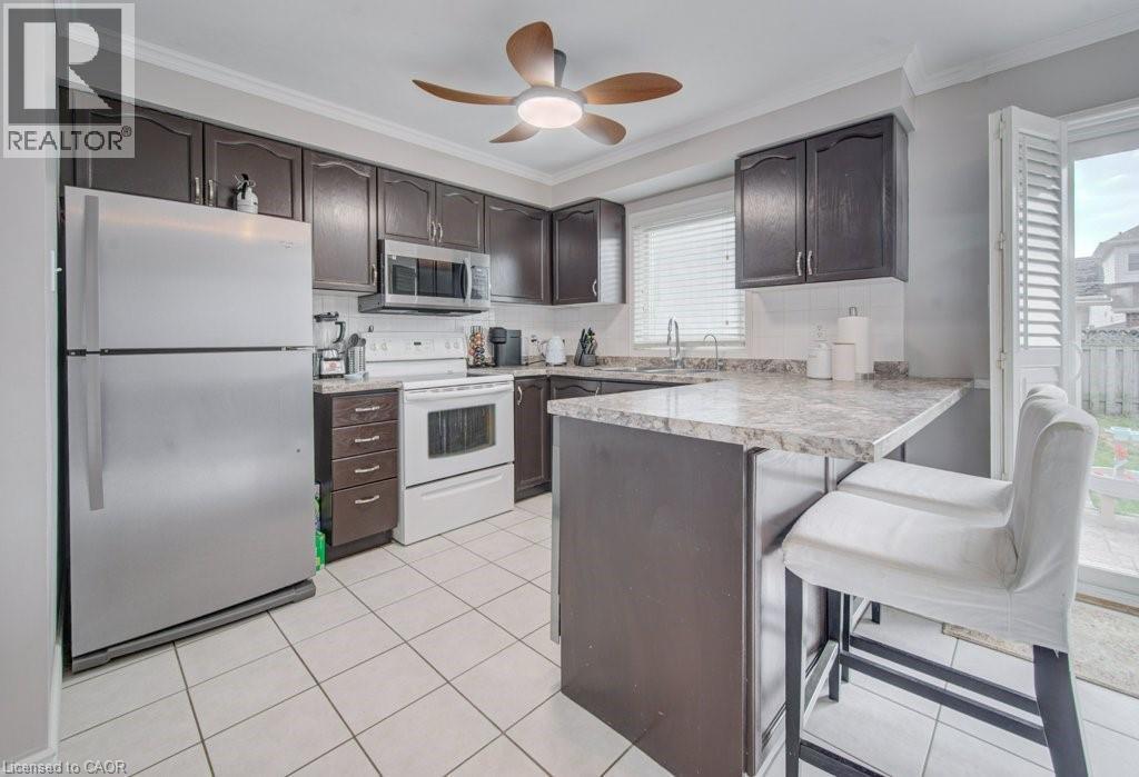 Kitchen featuring dark wood-finish cabinetry, stainless steel appliances, a breakfast bar, and white tile flooring - 334 Christopher Drive, Cambridge, ON - Indoor Photo Showing Kitchen