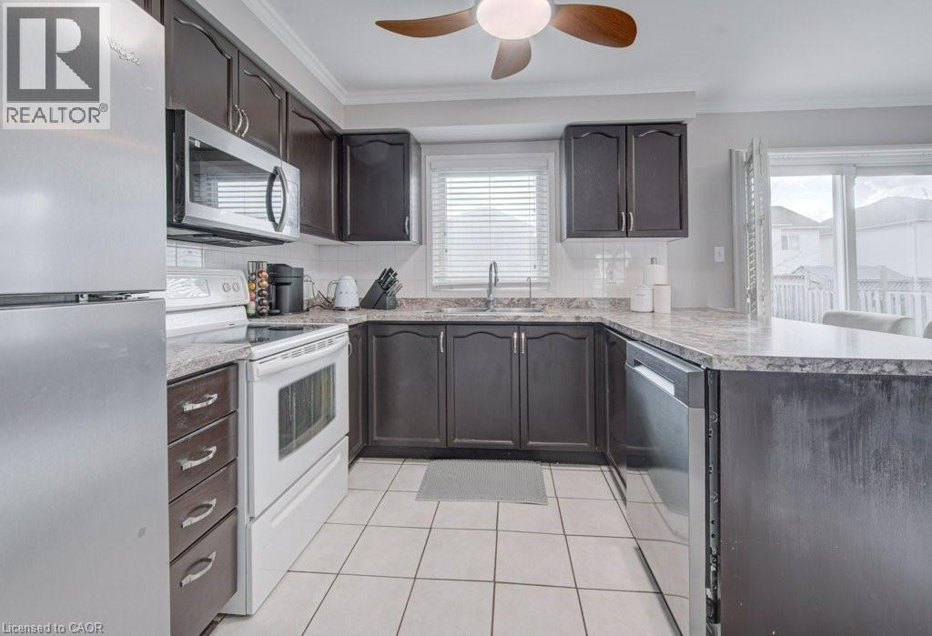 U-shaped kitchen featuring dark wood-finish cabinetry, light-toned countertops, and white tile flooring - 334 Christopher Drive, Cambridge, ON - Indoor Photo Showing Kitchen