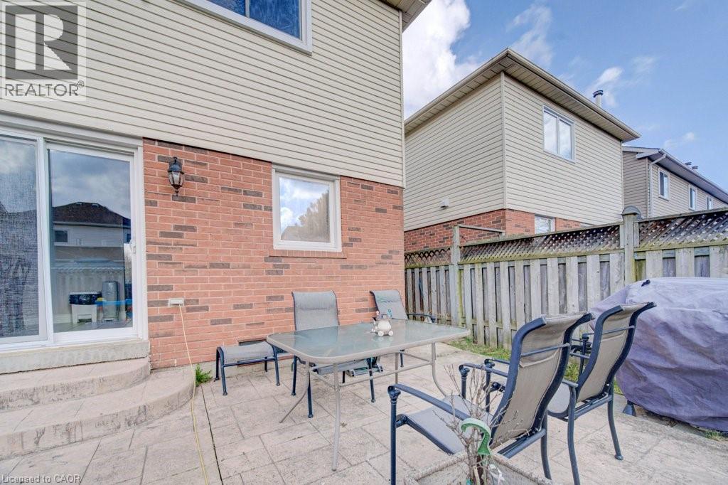 Rear exterior featuring a stamped concrete patio, red brick and horizontal siding facade, sliding glass patio door, exterior wall light fixture, and perimeter fencing - 334 Christopher Drive, Cambridge, ON - Outdoor With Deck Patio Veranda With Exterior