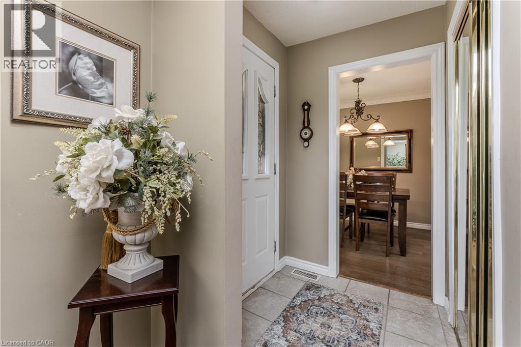 Warm entry foyer with tile flooring leading to a dining area featuring wood-finish flooring and a decorative chandelier - 643 Artreva Crescent, Burlington, ON - Indoor Photo Showing Other Room