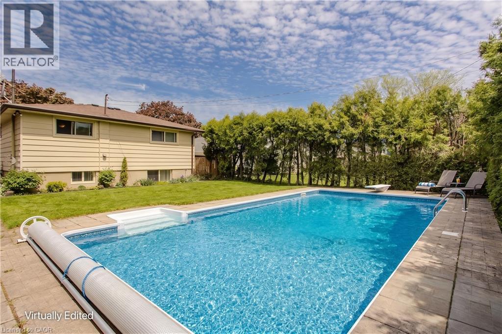 In-ground swimming pool with integrated steps, surrounded by stone paver decking and mature privacy landscaping - 643 Artreva Crescent, Burlington, ON - Outdoor With In Ground Pool With Backyard