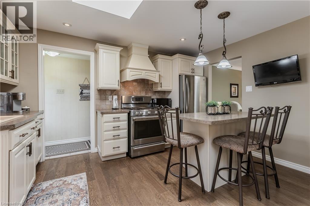 Kitchen featuring warm wood-finish flooring, light-toned cabinetry, stainless steel appliances, a built-in range hood, and a functional island with pendant lighting - 643 Artreva Crescent, Burlington, ON - Indoor Photo Showing Kitchen With Stainless Steel Kitchen With Upgraded Kitchen