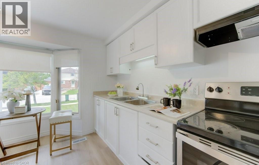 White cabinetry kitchen featuring a dual-basin stainless steel sink, light-toned countertops, and a stainless steel electric range with an overhead vent - 603 Pinerow Crescent Unit# B, Waterloo, ON - Indoor Photo Showing Kitchen With Double Sink