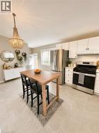 Open-concept kitchen featuring light-toned tile flooring, white cabinetry, and stainless steel appliances -