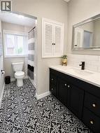 Bathroom featuring patterned black and white floor tiles, a black vanity with gold hardware, a white countertop with an integrated sink, a black faucet, and a white subway tile backsplash -