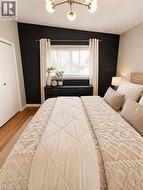 Bedroom featuring a contemporary ceiling fixture, a window with blinds and drapes, and wood-finish flooring -