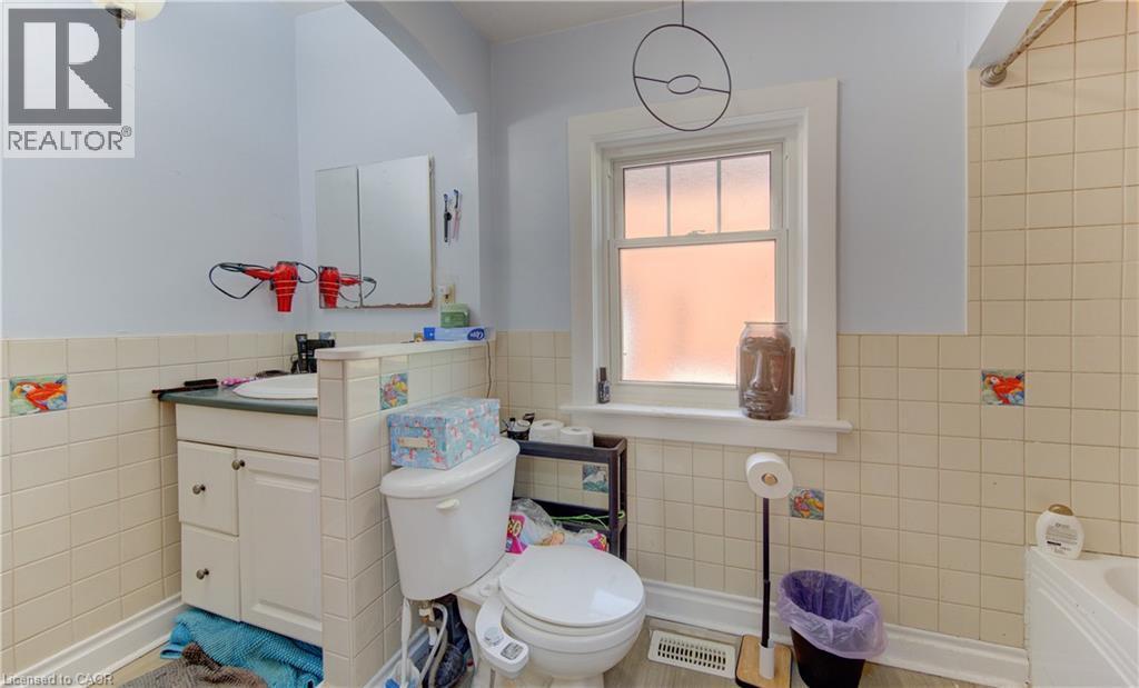 Main floor bathroom featuring light-toned wall tile with decorative accents, a single window, and a built-in vanity with under-sink storage - 48 Breithaupt Street, Kitchener, ON - Indoor Photo Showing Bathroom