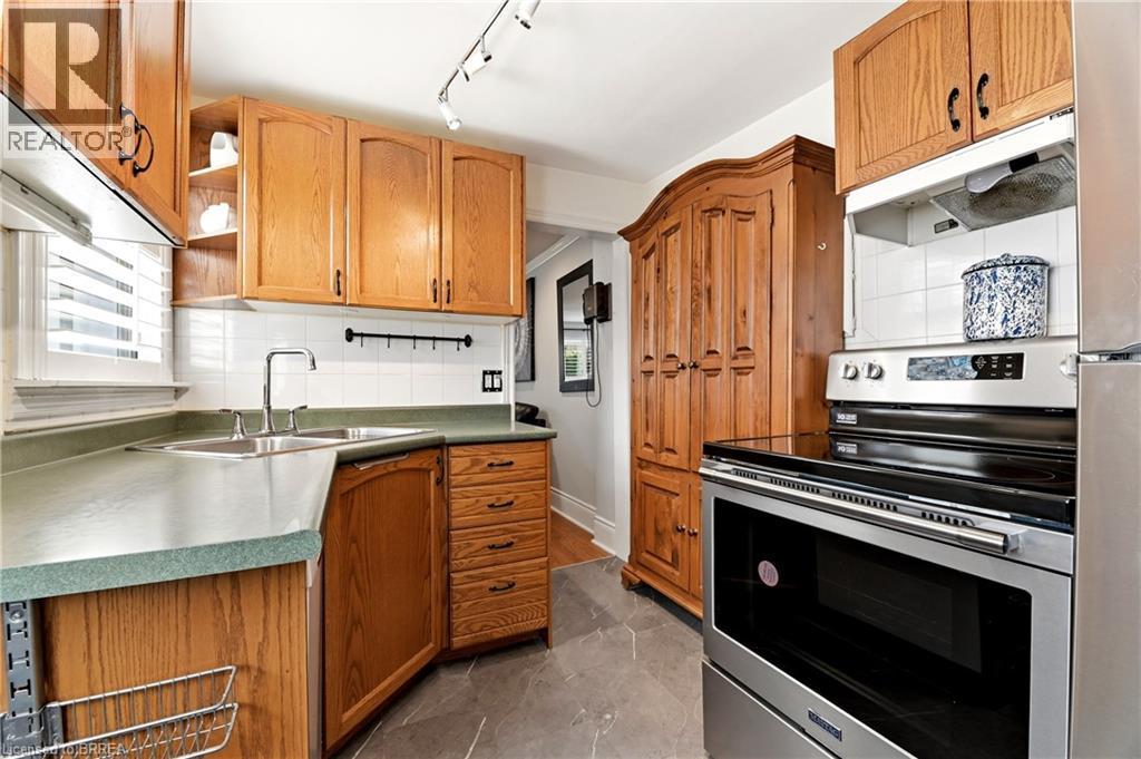 Kitchen featuring wood cabinetry, stainless steel appliances, a double basin sink, white tile backsplash, and slate-finish flooring - 23 Britannia Avenue, Hamilton, ON - Indoor Photo Showing Kitchen With Double Sink