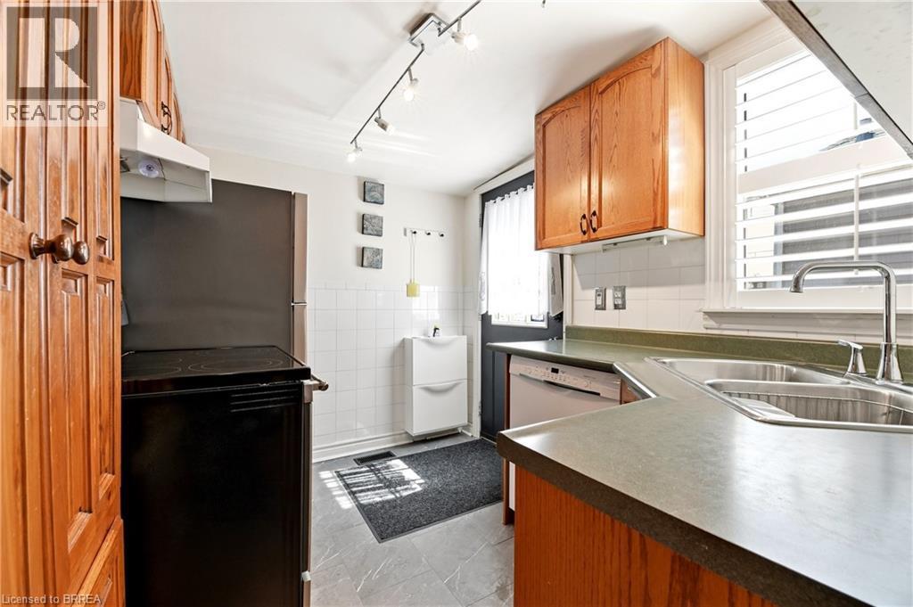 Kitchen featuring wood-finish cabinetry, solid surface countertops, a double basin stainless steel sink, and a built-in dishwasher - 23 Britannia Avenue, Hamilton, ON - Indoor Photo Showing Kitchen With Double Sink