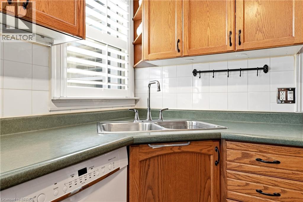 Kitchen featuring wood cabinetry, a double basin stainless steel sink with a chrome faucet, and a white tile backsplash - 23 Britannia Avenue, Hamilton, ON - Indoor Photo Showing Kitchen With Double Sink