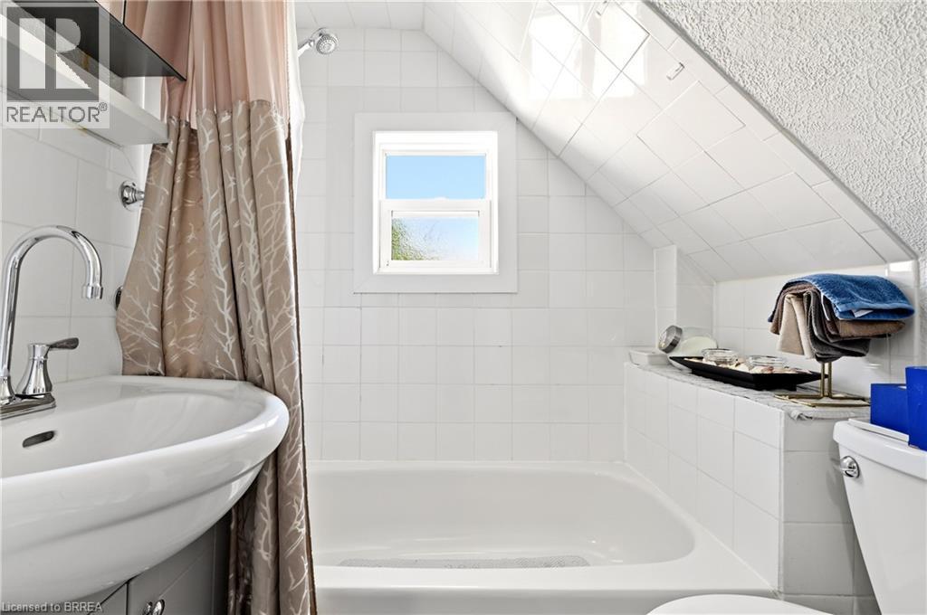 Bathroom featuring white subway tile walls, a built-in bathtub with shower, and a white vanity with a chrome faucet - 23 Britannia Avenue, Hamilton, ON - Indoor Photo Showing Bathroom
