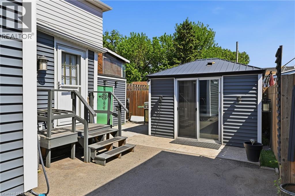 Rear yard area featuring a detached structure with sliding glass doors and a metal roof, alongside a separate building entrance with steps - 23 Britannia Avenue, Hamilton, ON - Outdoor