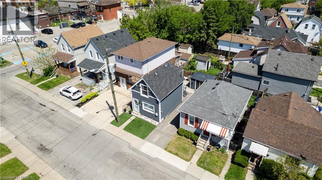 Aerial perspective showcasing residential properties with a mix of architectural styles, including a gray-sided home with white trim and a contrasting red and white striped awning - 23 Britannia Avenue, Hamilton, ON - Outdoor