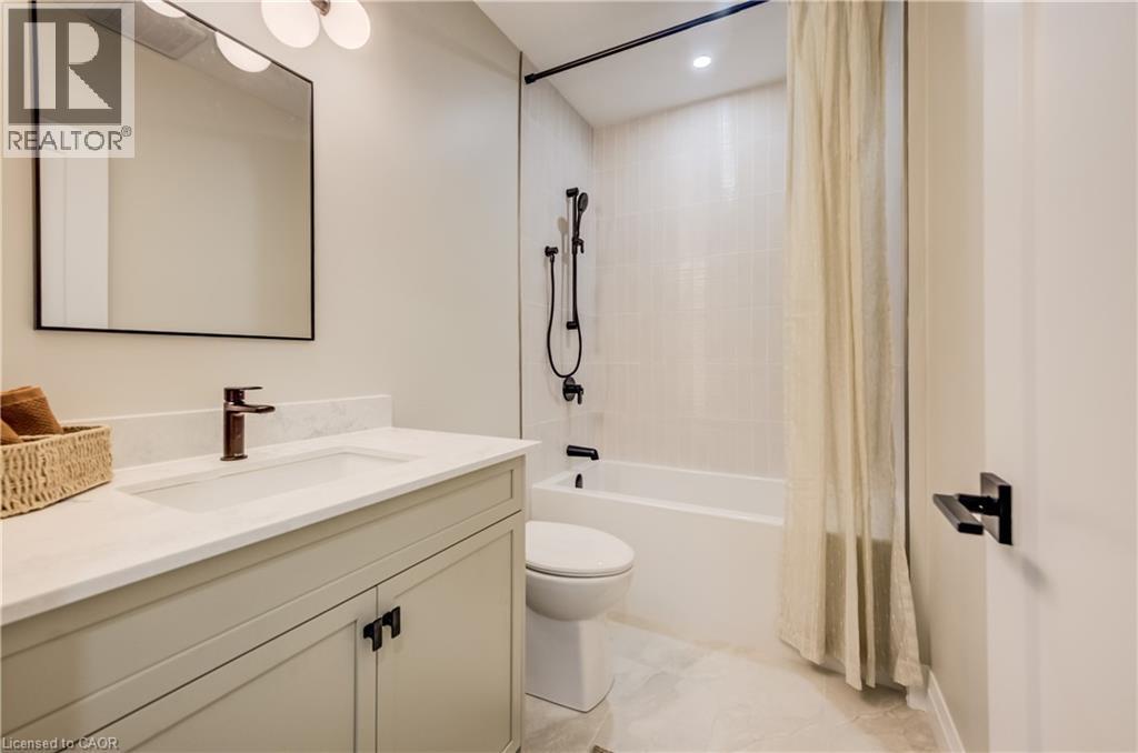 Bathroom featuring a light-toned vanity with a built-in sink, dark bronze hardware, a framed mirror, and a full bathtub with a tiled surround - 210 Heritage Drive Unit# Main, Kitchener, ON - Indoor Photo Showing Bathroom