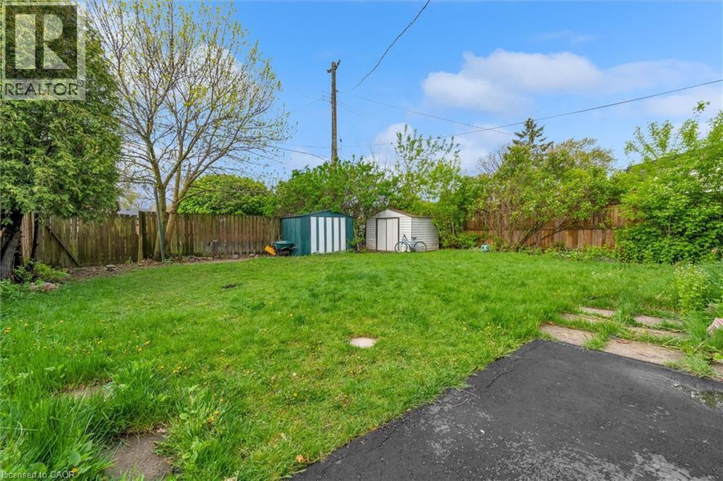 Expansive grassy yard featuring a wood fence, mature trees, a small storage shed, and a metal storage shed - 46 Beaconsfield Drive, Hamilton, ON - Outdoor