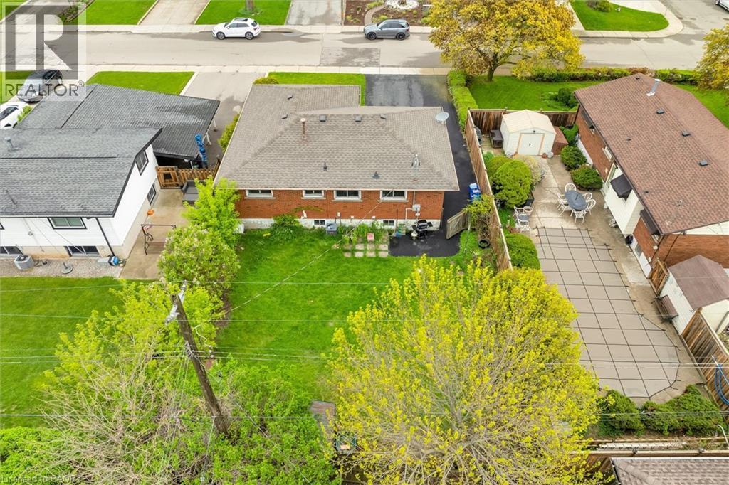 Rear exterior featuring a sizable backyard with a manicured lawn, a paved patio area, and mature trees - 46 Beaconsfield Drive, Hamilton, ON - Outdoor With View