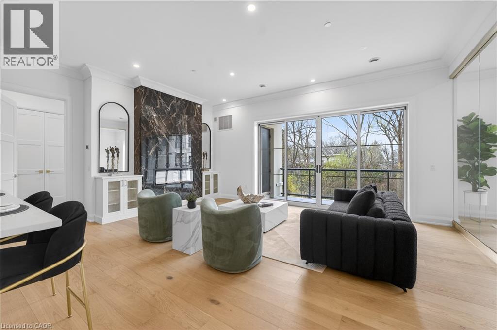Spacious living area featuring light wood-finish flooring, a full-height dark marble-look accent wall, and recessed ceiling lighting - 2 Arbourvale Common Unit# 209, St. Catharines, ON - Indoor Photo Showing Living Room