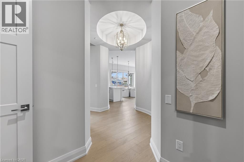 Hallway featuring wood-finish flooring, a tray ceiling with a hanging fixture, and white baseboards - 2 Arbourvale Common Unit# 209, St. Catharines, ON - Indoor Photo Showing Other Room