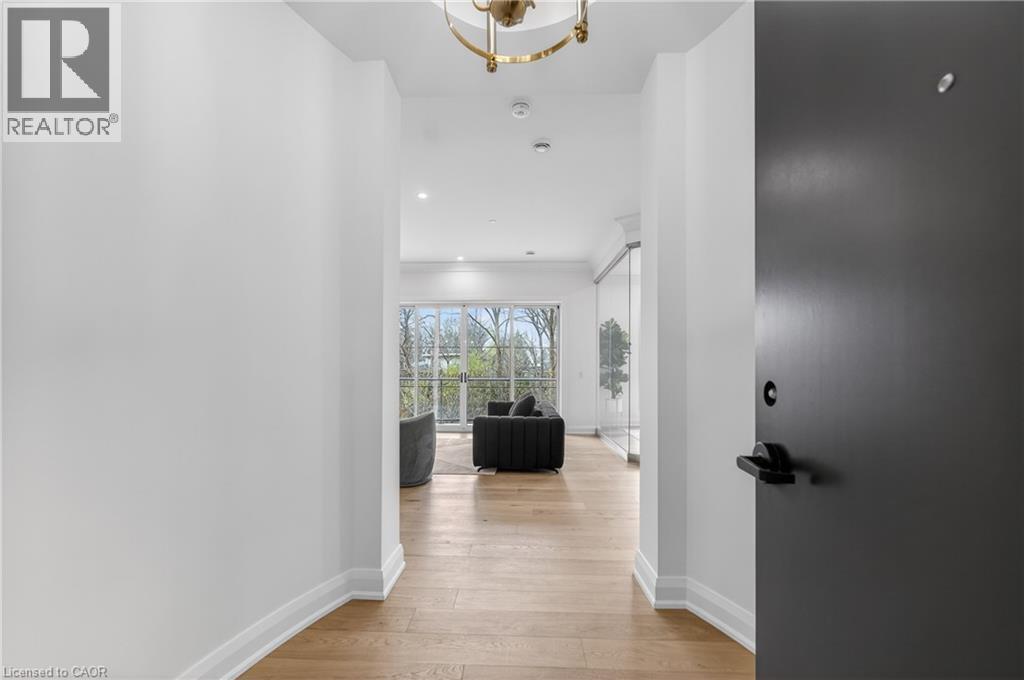 Entryway featuring a dark gray door with matte black hardware, leading to a space with wood-finish flooring, white walls, and a recessed lighting - 2 Arbourvale Common Unit# 209, St. Catharines, ON - Indoor Photo Showing Other Room