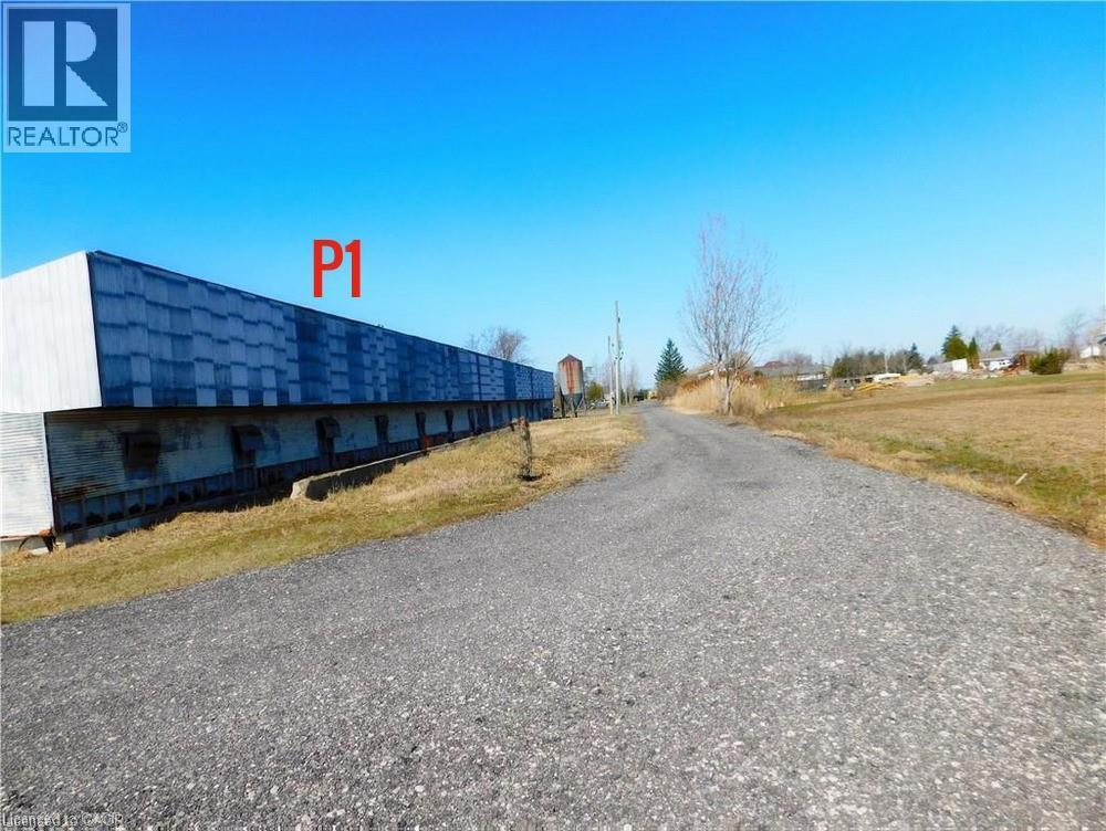Long commercial structure with a corrugated metal facade, featuring multiple lower-level openings, positioned alongside a gravel access road - 96 Second Road E, Stoney Creek, ON