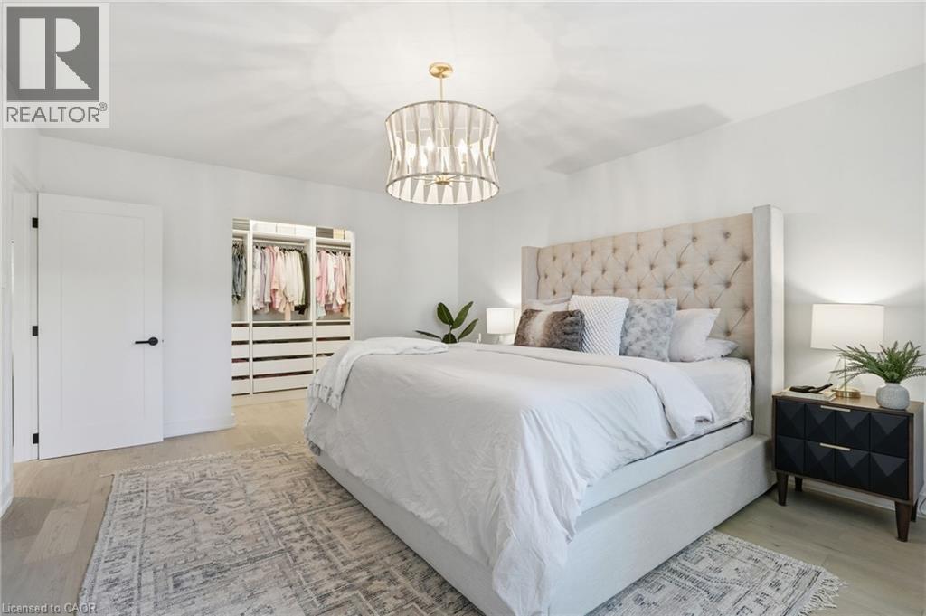 Spacious bedroom featuring light wood-finish flooring, a contemporary chandelier, a built-in custom closet system, and a white paneled door with matte black hardware - 345 Rankin Drive, Burlington, ON - Indoor Photo Showing Bedroom