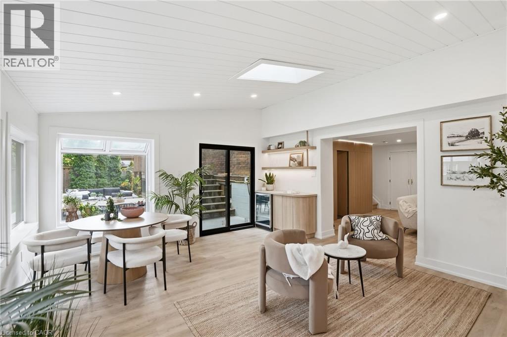 Open-concept living space with light wood-finish flooring, white shiplap ceiling, recessed lighting, and a large window overlooking exterior greenery - 345 Rankin Drive, Burlington, ON - Indoor