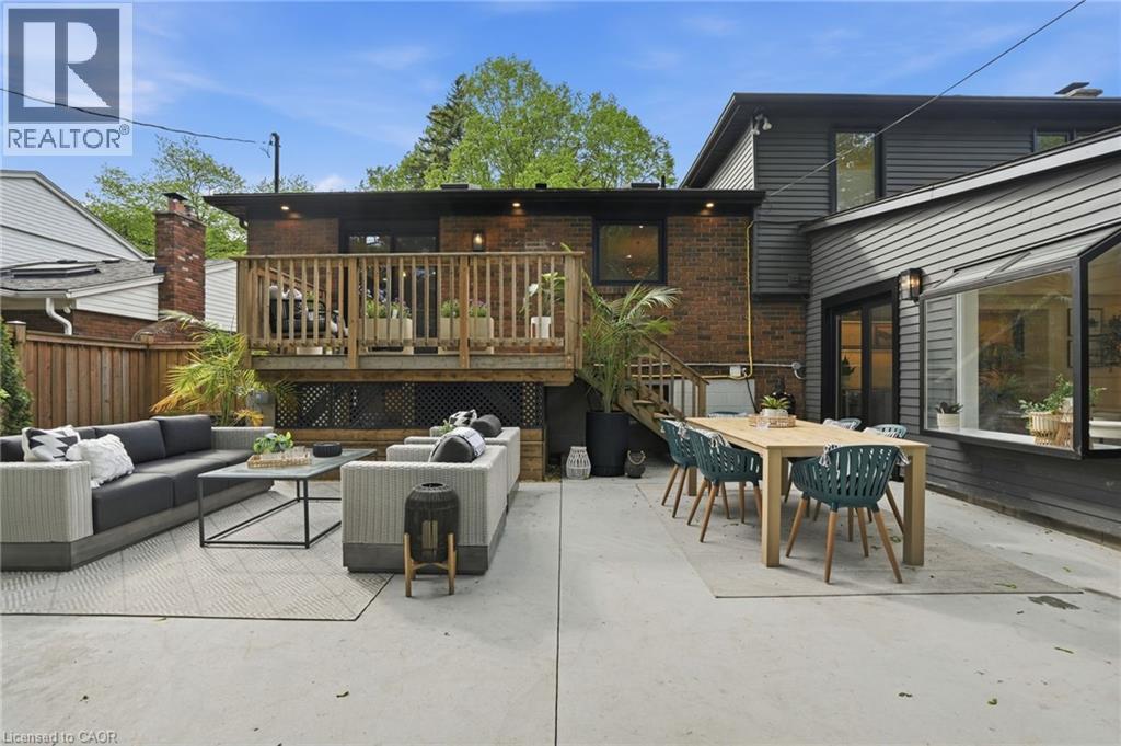 Spacious concrete patio with dual outdoor living areas, including a dining space with a large table and an additional seating area - 345 Rankin Drive, Burlington, ON - Outdoor With Deck Patio Veranda With Exterior