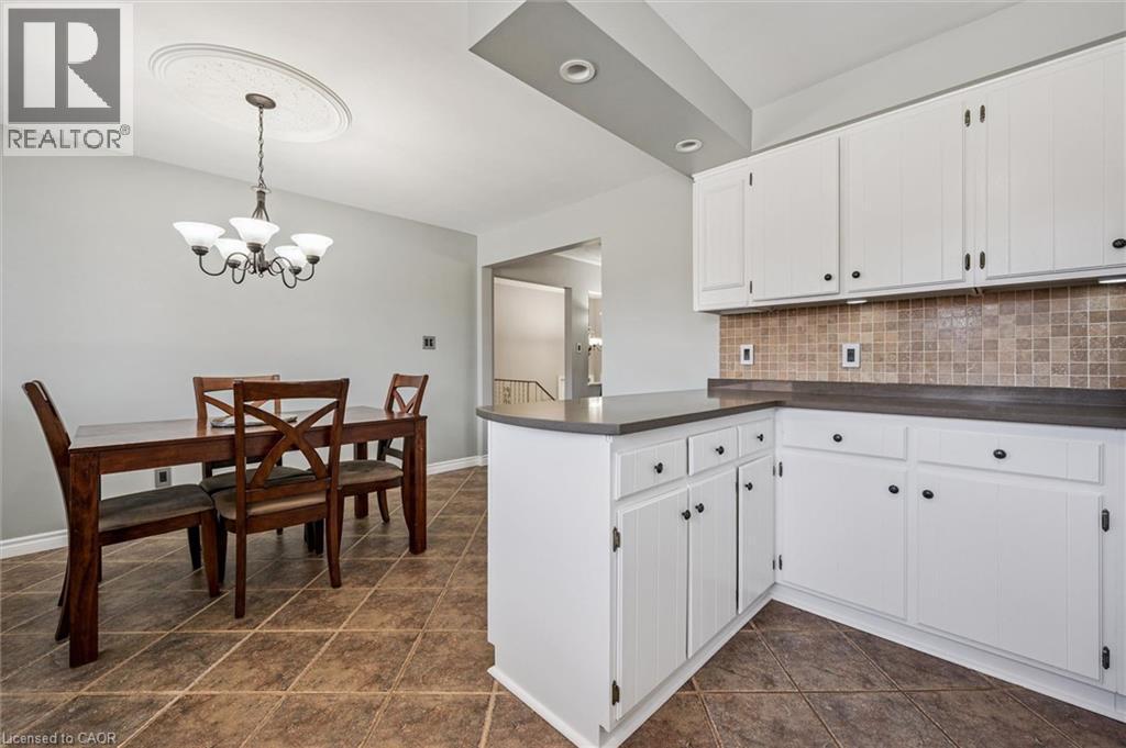 Open kitchen and dining area featuring white cabinetry, dark countertops, tiled backsplash, and ceramic tile flooring - 47 Oakhurst Crescent, Kitchener, ON - Indoor