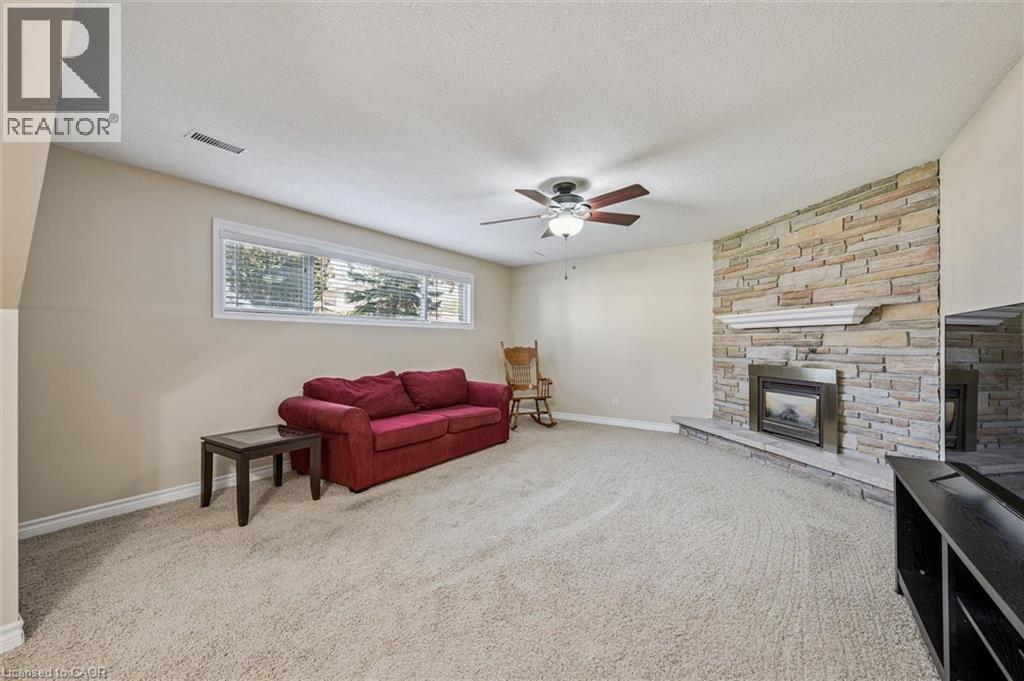 Spacious room featuring a stacked stone fireplace with a hearth and mantel, large horizontal windows, and a ceiling fan with integrated lighting - 47 Oakhurst Crescent, Kitchener, ON - Indoor Photo Showing Living Room With Fireplace