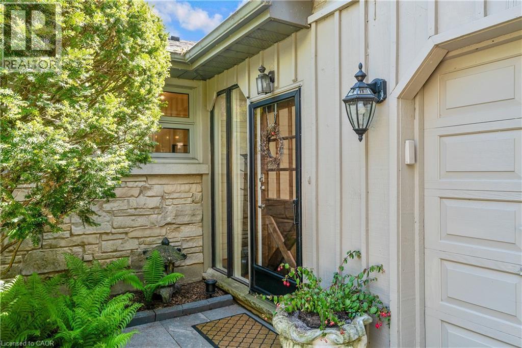 Stone veneer and vertical panel siding exterior featuring a paneled garage door, a full-light entry door, and an exterior lantern sconce - 91 Limerick Drive, Kitchener, ON - Outdoor With Exterior