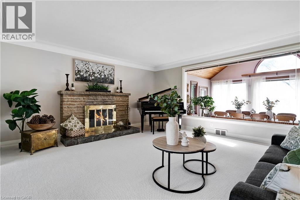 Spacious living area featuring a stone fireplace with a brass firebox, crown molding, and light-colored carpeting - 91 Limerick Drive, Kitchener, ON - Indoor Photo Showing Living Room With Fireplace