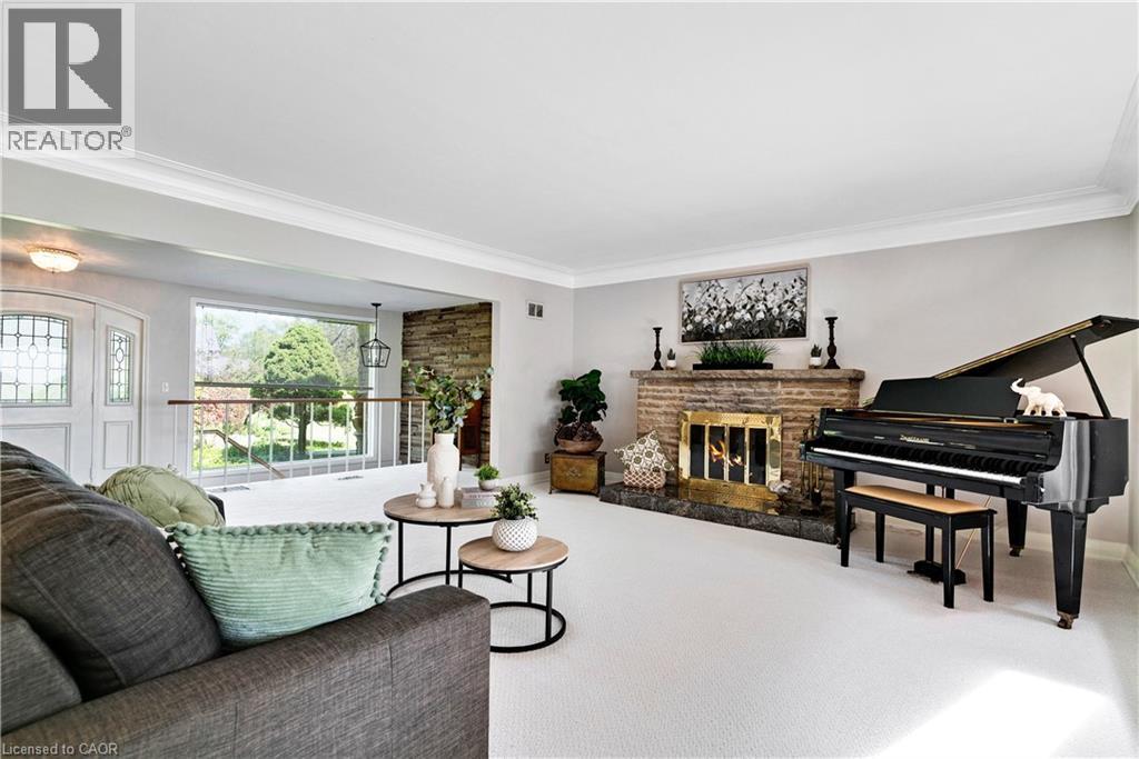 Living area featuring a stone-clad fireplace with a brass firebox, white carpeting, and crown molding - 91 Limerick Drive, Kitchener, ON - Indoor With Fireplace