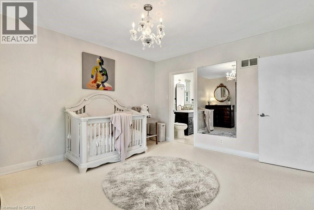 Carpeted room with a crystal chandelier, white walls, and an open doorway leading to an attached bathroom - 91 Limerick Drive, Kitchener, ON - Indoor Photo Showing Bedroom