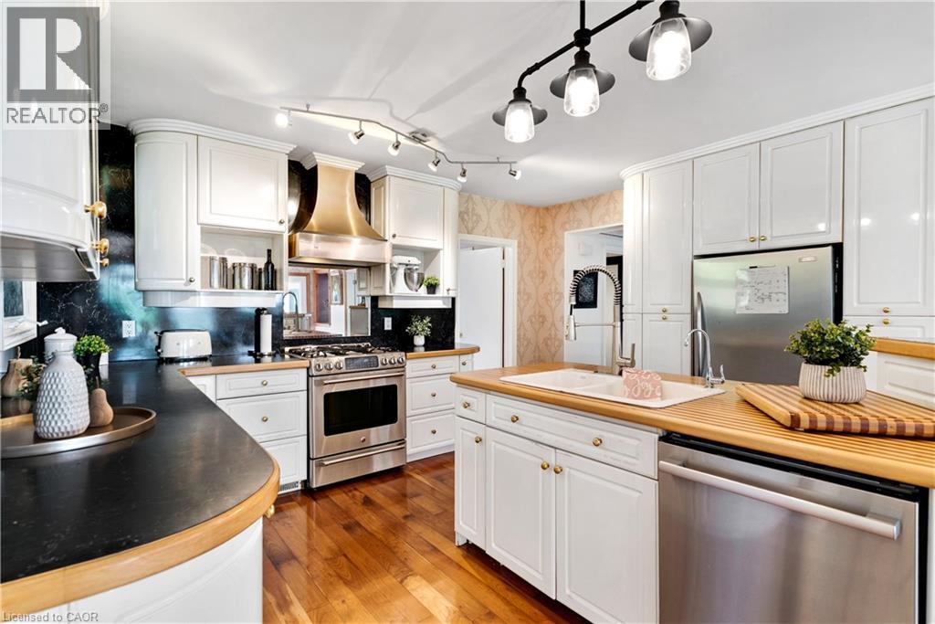Kitchen featuring white cabinetry, stainless steel appliances, wood-finish flooring, dark countertops, and a central island with a built-in sink - 91 Limerick Drive, Kitchener, ON - Indoor Photo Showing Kitchen