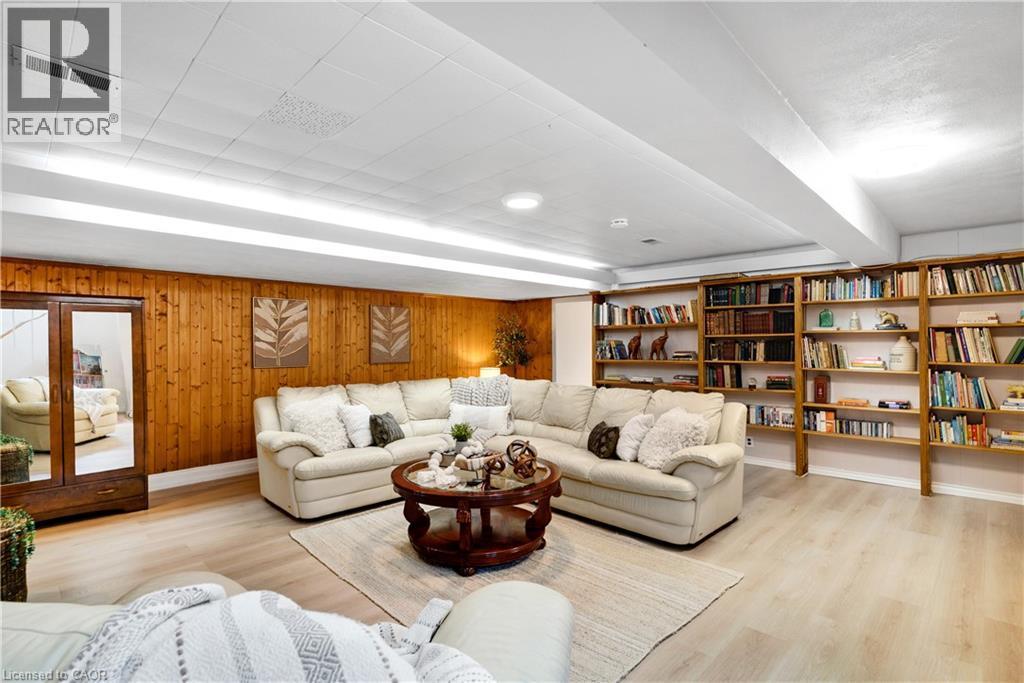 Recreation room featuring wood paneling, extensive built-in shelving, wood-finish flooring, and a drop ceiling with integrated strip lighting and recessed fixtures - 91 Limerick Drive, Kitchener, ON - Indoor Photo Showing Living Room