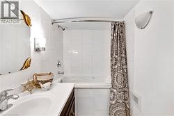 Bathroom featuring a white tile shower surround, built-in bathtub, chrome shower fixture, and a vanity with an undermount sink -