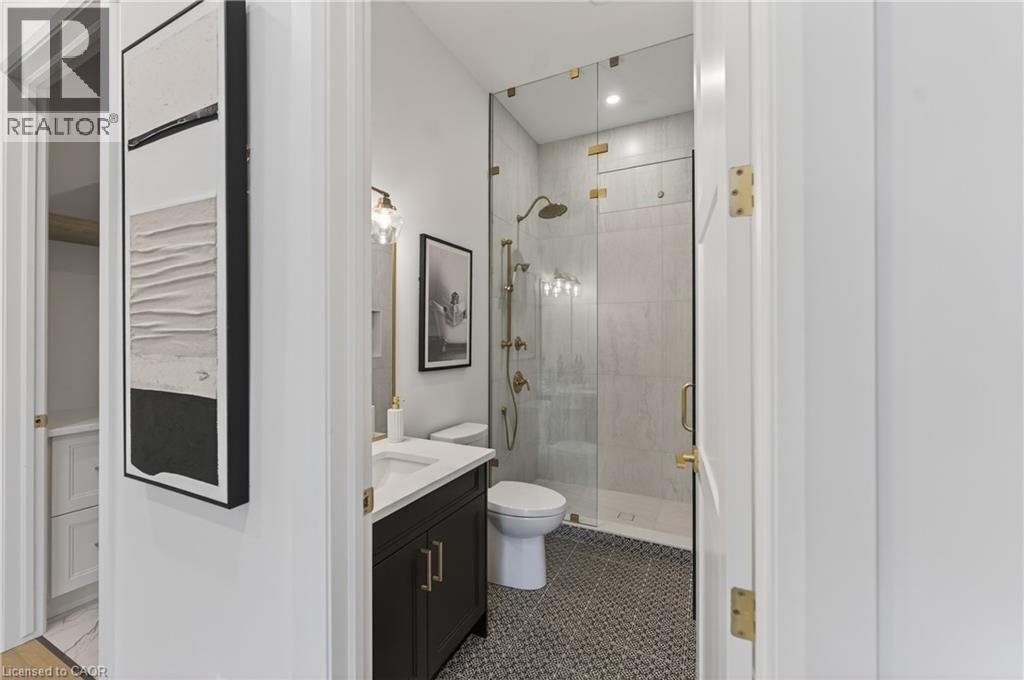 Bathroom featuring a glass-enclosed shower with gold-tone fixtures, a dark wood-finish vanity with a white countertop, and mosaic tile flooring - 2 Arbourvale Common Unit# 410, St. Catharines, ON - Indoor Photo Showing Bathroom