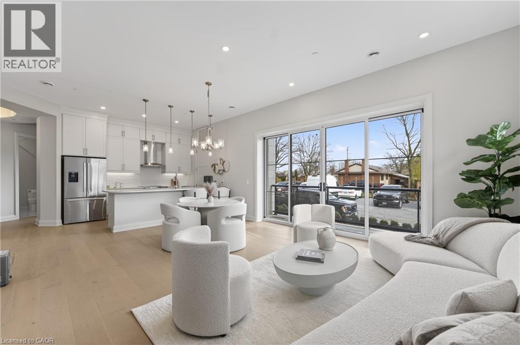 Open-concept living area featuring light wood-finish flooring, recessed lighting, and a modern kitchen with stainless steel appliances - 2 Arbourvale Common Unit# 410, St. Catharines, ON - Indoor Photo Showing Other Room