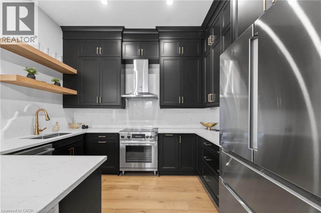 Modern kitchen featuring dark cabinetry, light countertops, stainless steel appliances, wood-finish flooring, and open shelving - 2 Arbourvale Common Unit# 410, St. Catharines, ON - Indoor Photo Showing Kitchen With Double Sink With Upgraded Kitchen