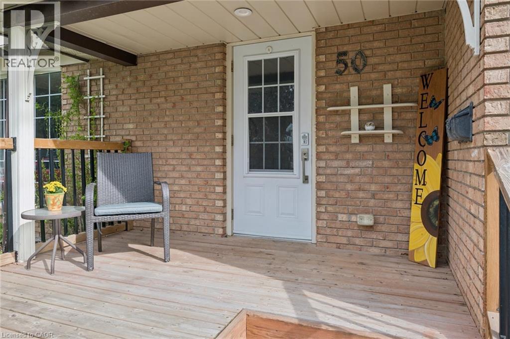 Brick exterior with a covered porch featuring a white entry door with glass inserts, a wood-finish deck, and black metal railings - 50 Lewis Crescent, Kitchener, ON - Outdoor With Deck Patio Veranda With Exterior