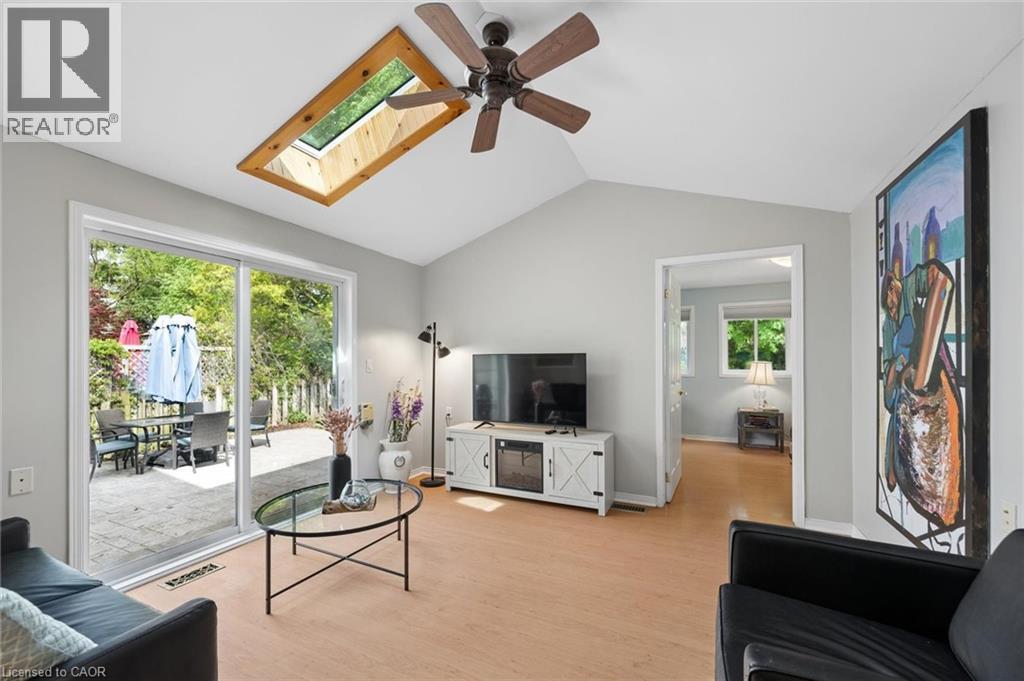 Vaulted ceiling with skylight and ceiling fan, light wood-finish flooring, sliding glass door to outdoor patio, and a light gray wall color - 50 Lewis Crescent, Kitchener, ON - Indoor Photo Showing Living Room