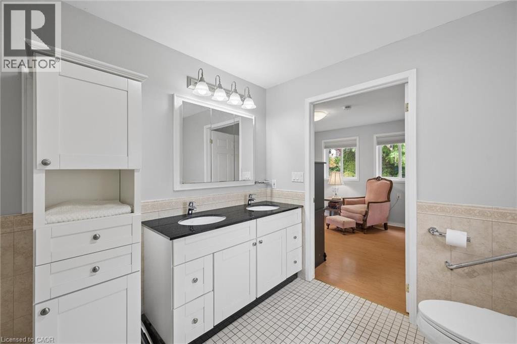 Bathroom featuring a dual-sink vanity with a dark countertop and white cabinetry, a built-in linen tower, white tile flooring, and a tiled half-wall - 50 Lewis Crescent, Kitchener, ON - Indoor Photo Showing Bathroom