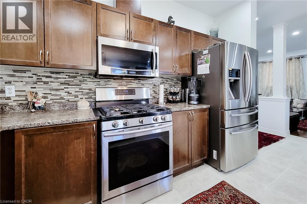 Kitchen featuring wood cabinetry, stainless steel appliances, a mosaic tile backsplash, and light-toned flooring - 197 Cloverleaf Drive, Ancaster, ON - Indoor Photo Showing Kitchen