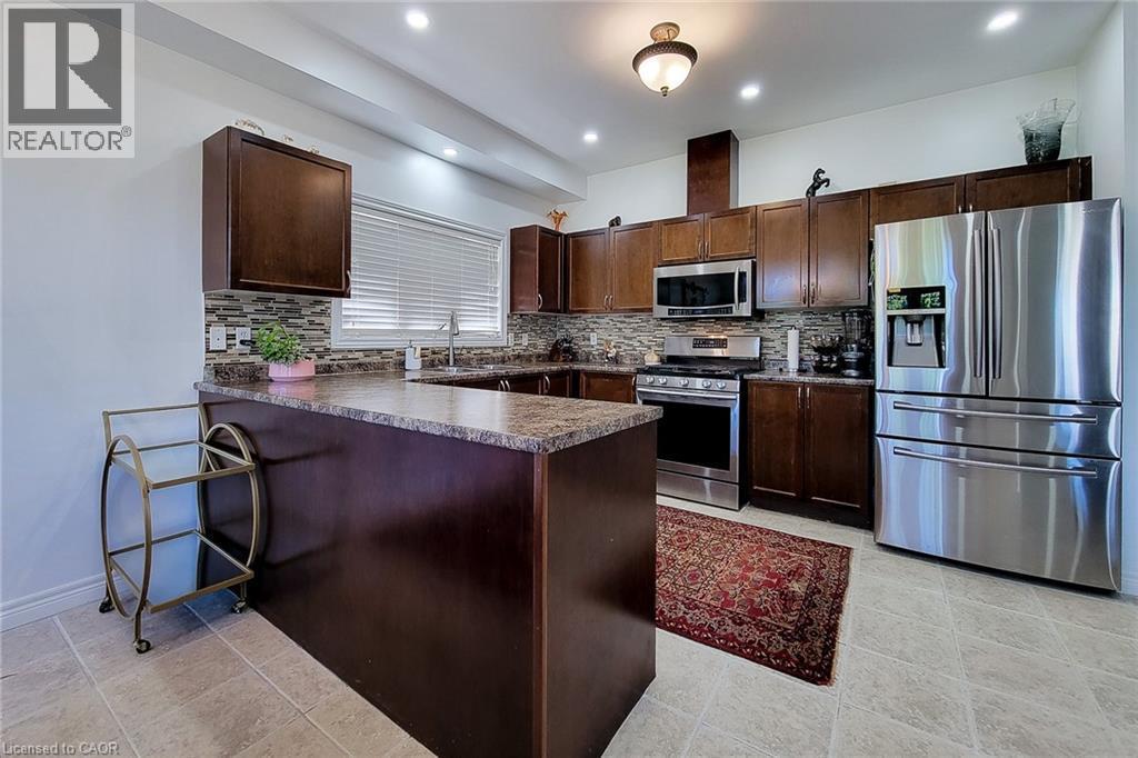 Kitchen featuring wood-finish cabinetry, stainless steel appliances, and a mosaic tile backsplash - 197 Cloverleaf Drive, Ancaster, ON - Indoor Photo Showing Kitchen With Upgraded Kitchen