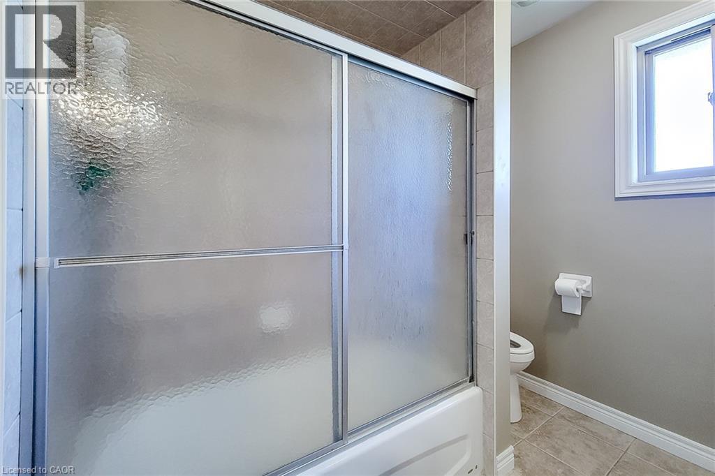 Bathtub with sliding textured glass doors, complemented by surrounding wall tile and a neutral paint palette - 197 Cloverleaf Drive, Ancaster, ON - Indoor Photo Showing Bathroom