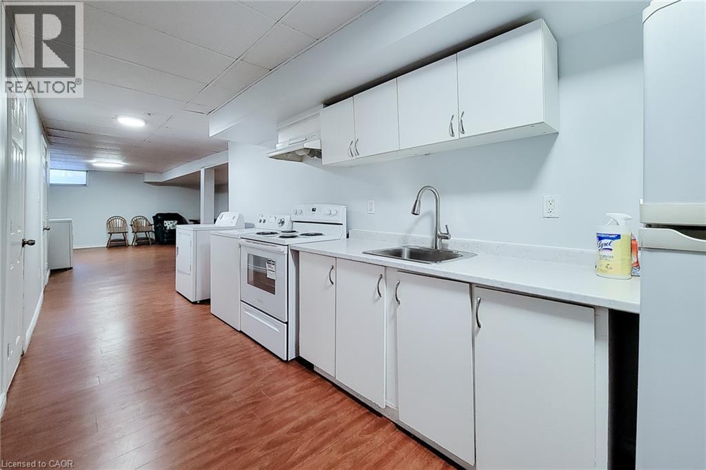 Functional kitchen area featuring white cabinetry, a stainless steel sink with a high-arc faucet, and white appliances including a range and refrigerator - 197 Cloverleaf Drive, Ancaster, ON - Indoor Photo Showing Kitchen