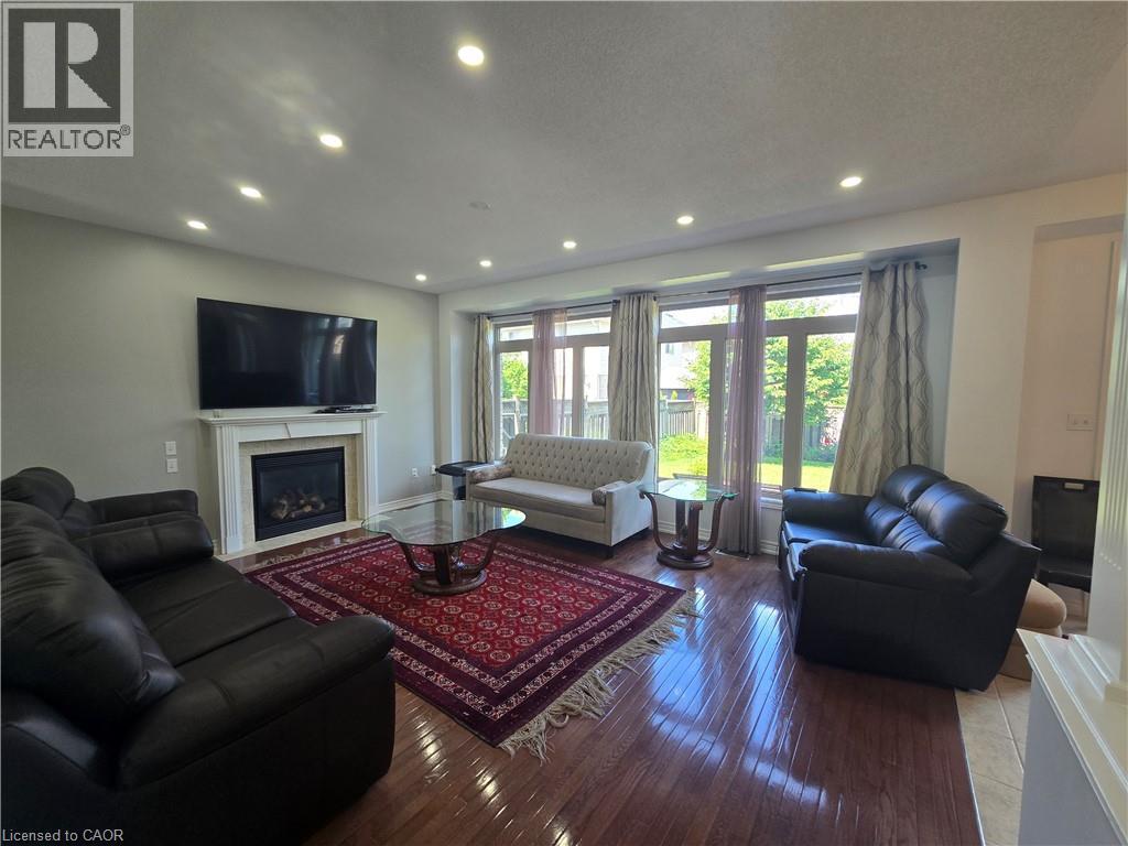 Living area featuring wood-finish flooring, a fireplace with a mantel, recessed lighting, and large windows overlooking exterior greenery - 197 Cloverleaf Drive, Ancaster, ON - Indoor Photo Showing Living Room With Fireplace