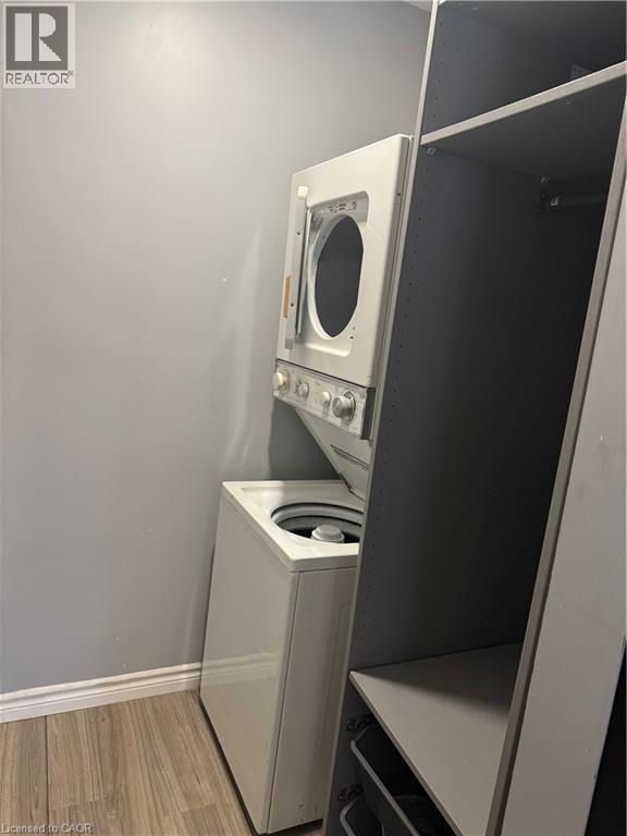 Dedicated laundry area featuring a stacked washer and dryer unit, wood-finish flooring, and light gray wall paint - 61 E Waterloo Drive Unit# 61, Kitchener, ON - Indoor Photo Showing Laundry Room