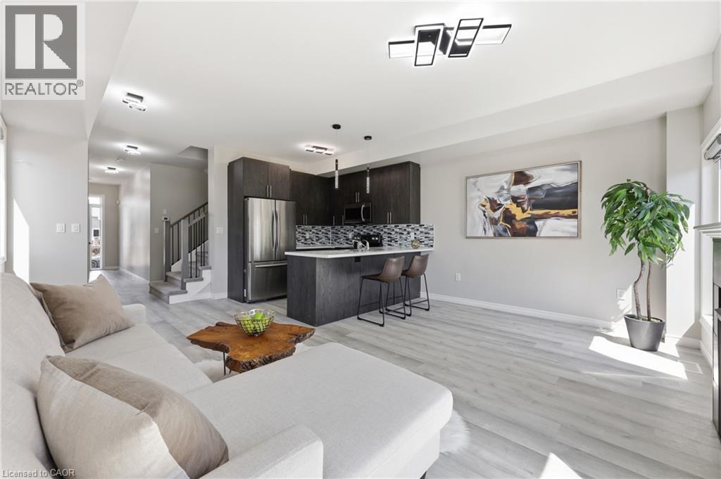 Open-concept living space featuring wood-finish flooring, a contemporary kitchen with dark cabinetry, stainless steel appliances, a breakfast bar, and modern overhead lighting - 37 Delena Avenue S, Hamilton, ON - Indoor